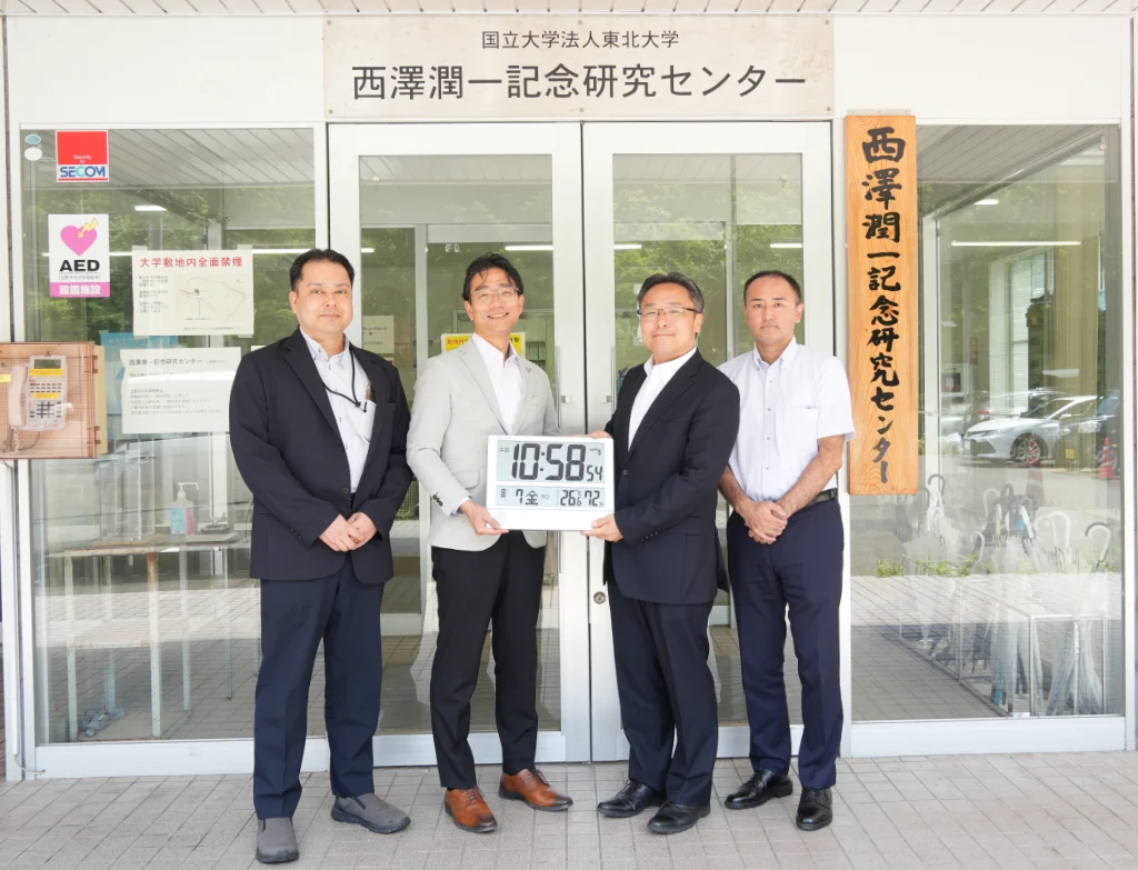 Associate Professor Masaaki Moriyama of Tohoku University’s μSIC; Professor Kentaro Totsu, Director of μSIC; and Tsukasa Kawabe, President of Samco Inc., with a digital clock commemorating Samco’s 5,000-system milestone.