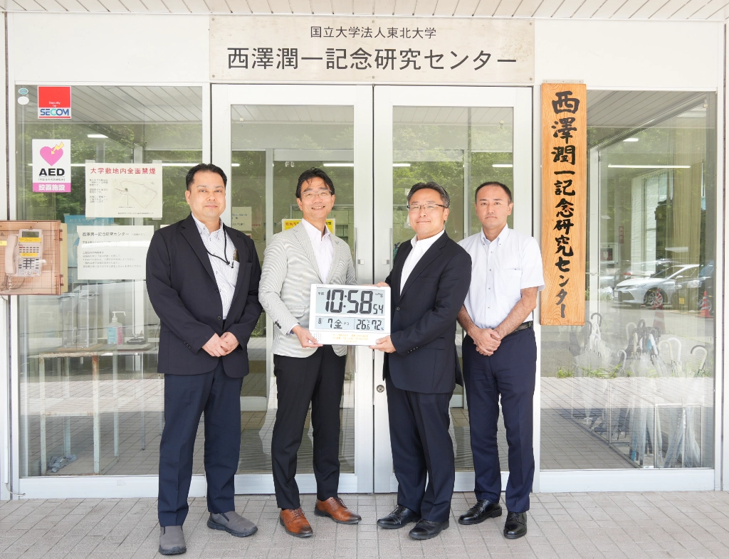 Associate Professor Masaaki Moriyama of Tohoku University’s μSIC; Professor Kentaro Totsu, Director of μSIC; and Tsukasa Kawabe, President of Samco Inc., with a digital clock commemorating Samco’s 5,000-system milestone.